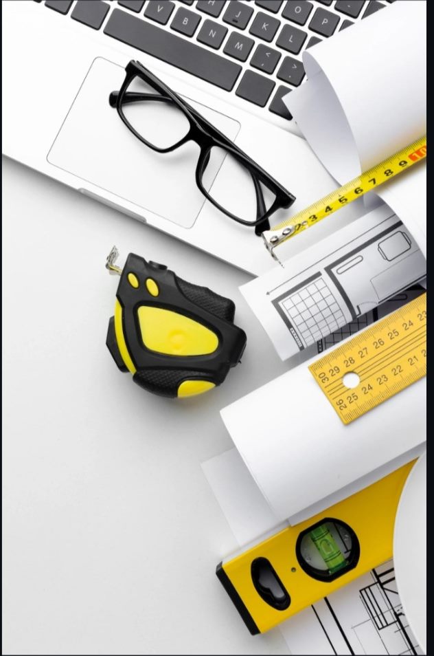 Portátil, gafas, flexómetro y nivel sobre planos de obra