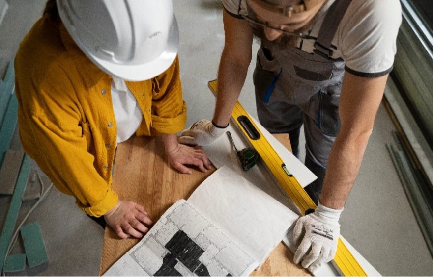 Dos trabajadores midiendo sobre un plano en obra